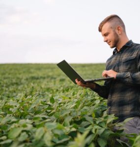 Homem no meio de uma lavoura de soja com um notebook